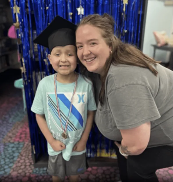 Wyatt with a graduation cap and medal standing next to a smiling woman.