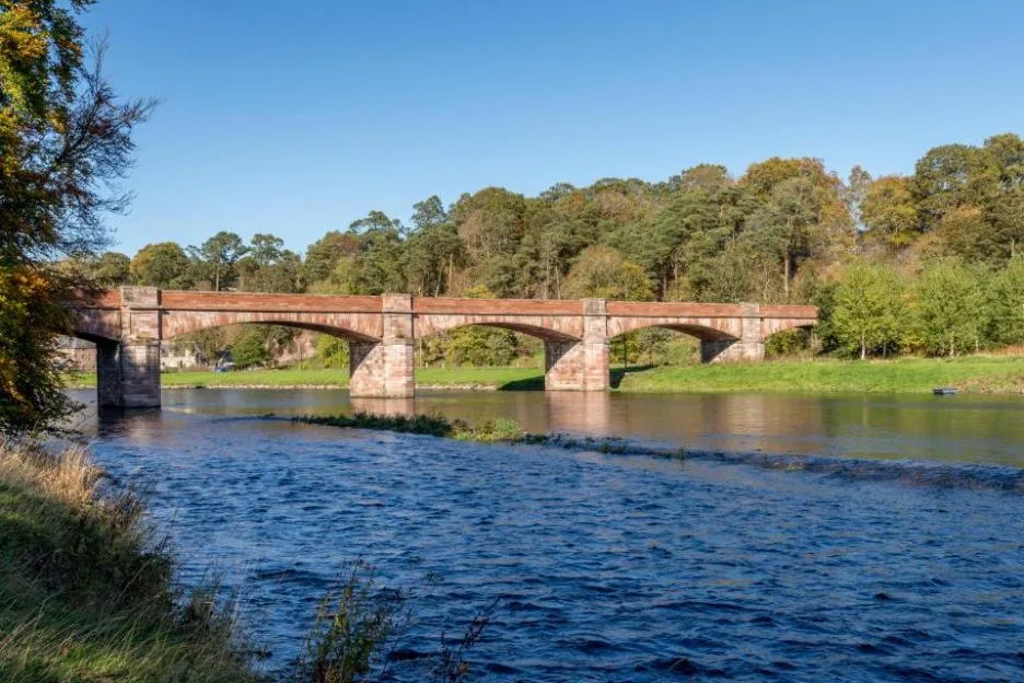 Mertoun Bridge across the River Tweed with trees and green banks.