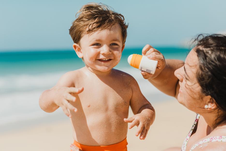 A mother applying sunscreen to her baby's face at the beach.