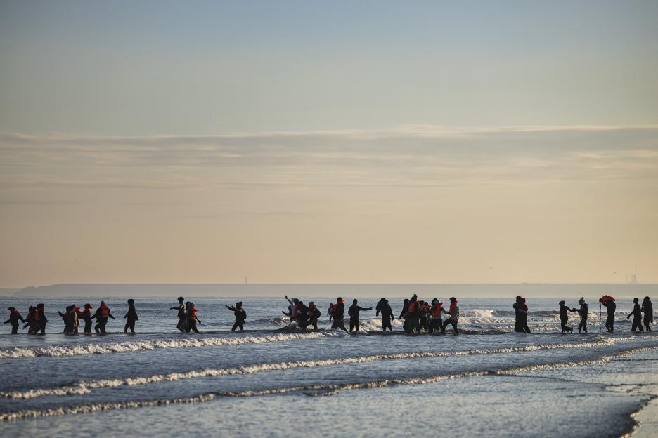Migrants wade into the sea wearing life vests to board smugglers' boats in an attempt to cross the English Channel.