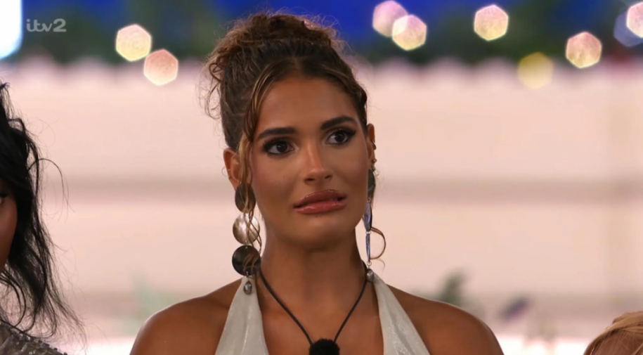 A woman with brown hair in an updo and large earrings looks away with a slight grimace.