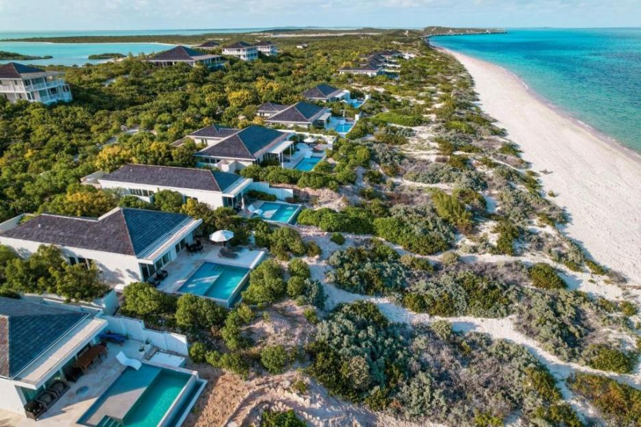 Aerial view of Sailrock South Caicos resort, showing villas with pools nestled among green trees along a white sand beach and turquoise ocean.