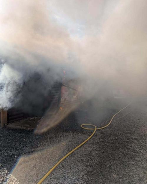 Firefighters spraying water on a building fire, creating a misty rainbow effect, with smoke billowing from the building.