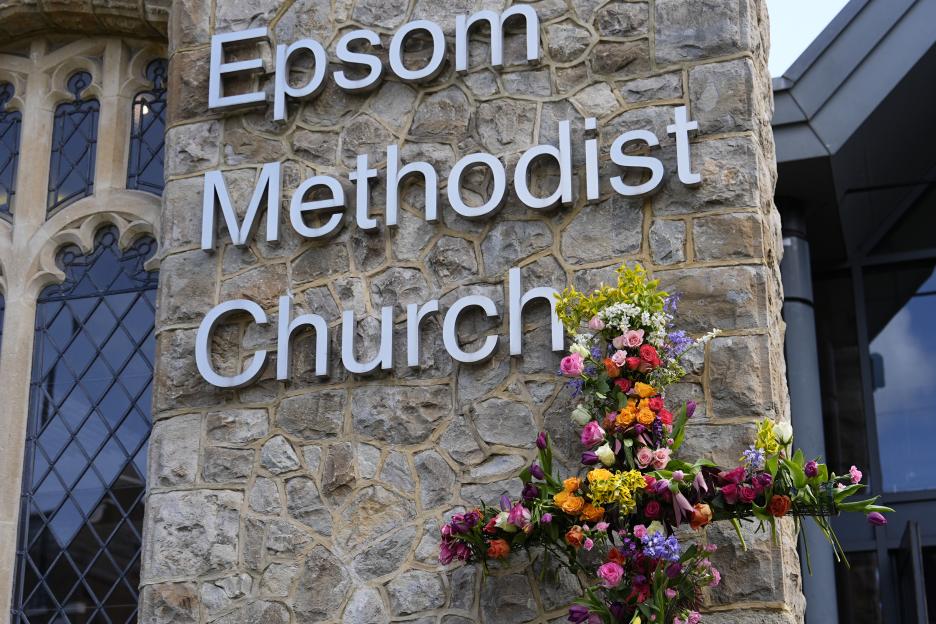 The sign for Epsom Methodist Church on an exterior stone wall, with a large floral cross below the sign.