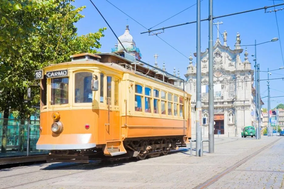 A vintage yellow and orange tramway in Porto, with the Igreja do Carmo e Carmelitas church in the background.