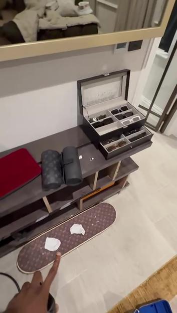 Room with an open jewelry box with glasses, two cylindrical cases, a red laptop, and a skateboard on the floor.
