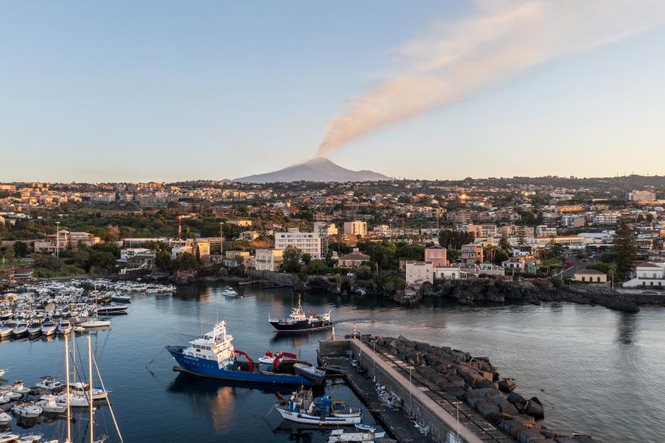 Mount Etna emits a plume of volcanic ash at dawn behind the harbor of Ognina in Catania, Italy.