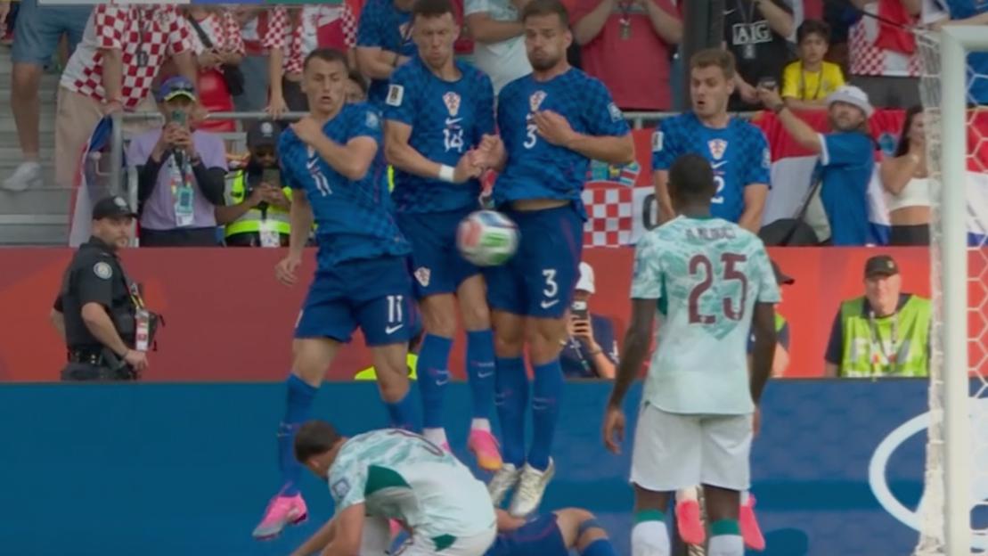 Four Croatian players jump to block a free-kick while another player lies behind them.