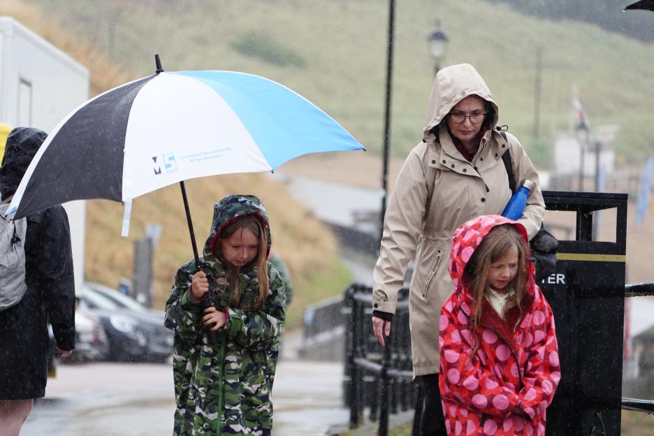 People shelter from the rain under an umbrella on the coast.