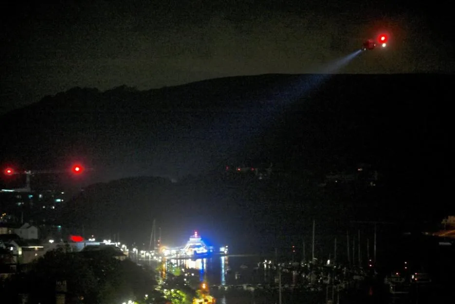 An air ambulance hovering over a town at night with its spotlight on.