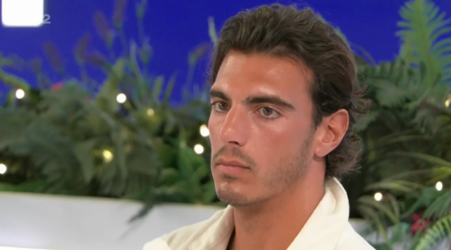 A man with dark hair and a tan wearing a white shirt looking to the left.