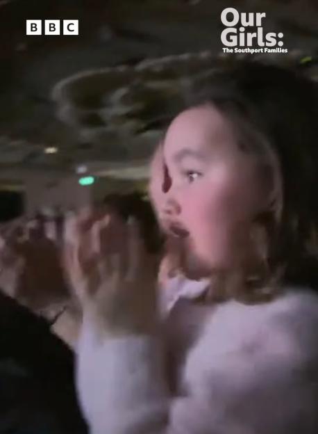 A young woman in a pale pink sweater claps and looks shocked, with text overlay "Our Girls: The Southport Families" and BBC promotional text.