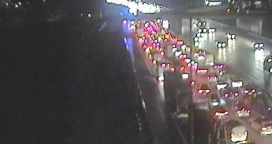 Nighttime aerial view of heavy traffic on a multi-lane highway, with red taillights and white headlights visible.