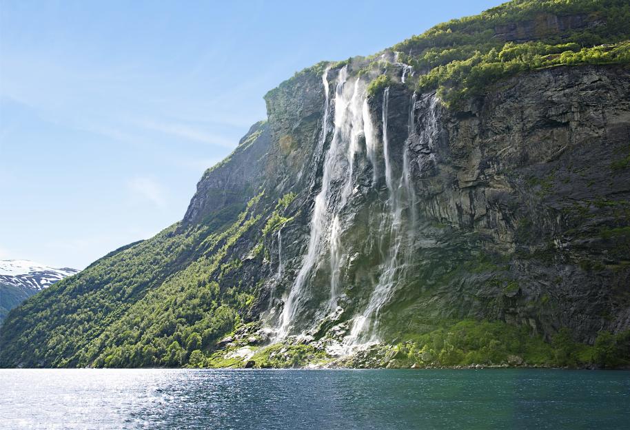 Waterfalls cascading down a rocky, forested mountain into a body of water.