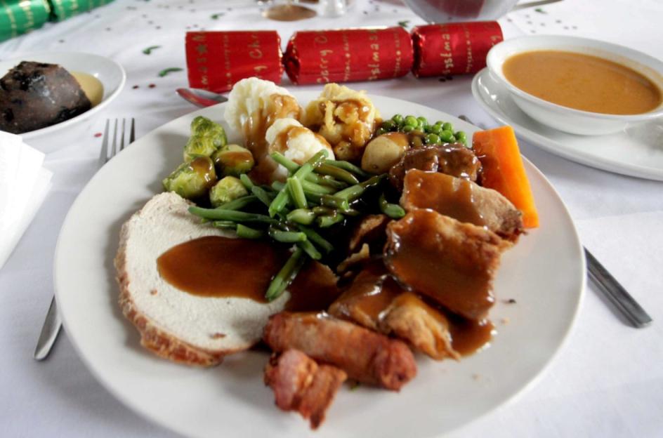 A Christmas dinner plate with turkey, vegetables, sausage, and gravy.