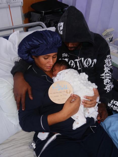 New parents hold their newborn baby, Cairo Kaycee Adjei-Waam, in a hospital bed.