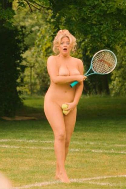 Emily Atack nude in a grassy area, holding a tennis racket and two tennis balls.
