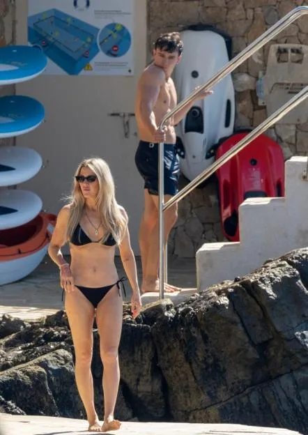 Ellie Goulding wearing a black bikini and sunglasses walks near the water while her boyfriend, Beau Minniear, stands on nearby steps in the South of France.