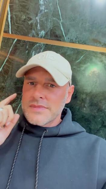 Lee Andrews, husband of Katie Price, wearing a cap and black hoodie, making a thinking gesture.