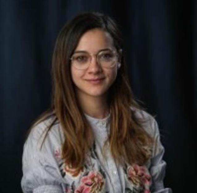 A young woman with brown hair, wearing glasses and a floral shirt, smiles.