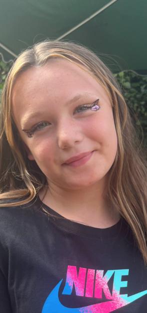 A young girl with blonde hair and butterfly wing eye makeup, smiling.