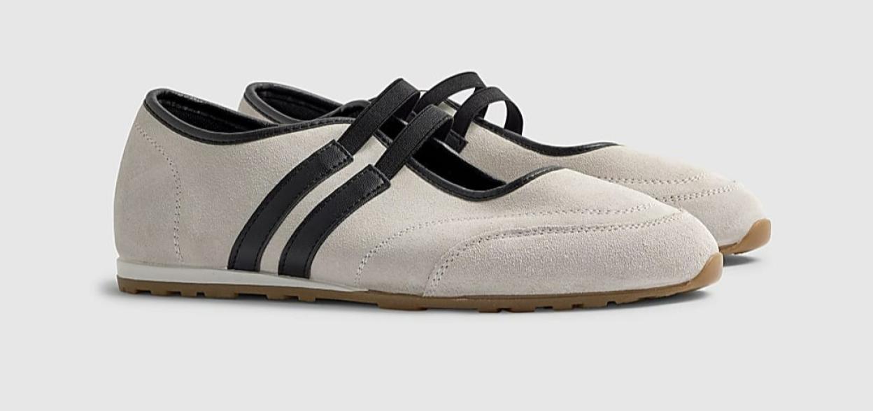 Pair of beige suede Mary Jane style flats with black straps.