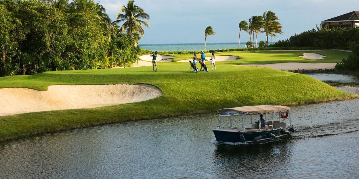 People playing golf at the Fairmount Mayakoba, Riviera Maya, with a boat passing by on a canal.