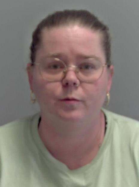 Mugshot of a woman with dark hair pulled back, wearing glasses, a nose ring, hoop earrings, and a light green t-shirt.