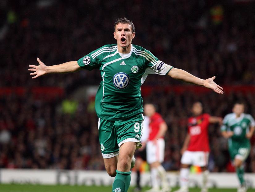 A soccer player in a green jersey celebrates a goal with arms outstretched.