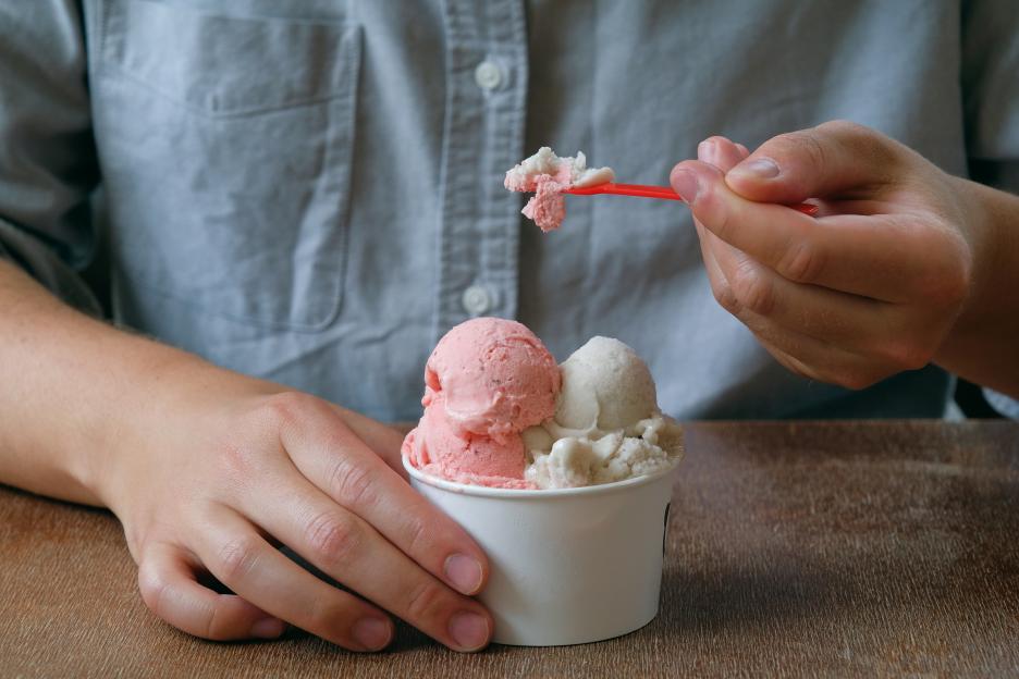A person holding a cup with two scoops of ice cream and a spoon with a small portion of ice cream.