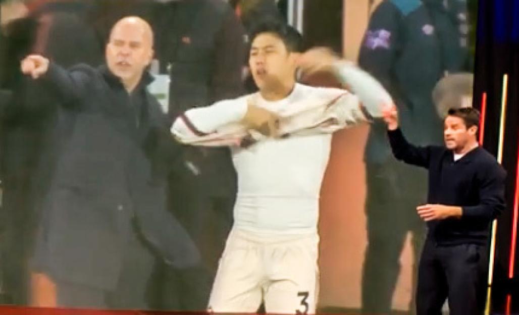 Man reacting to a sports video on a large screen, where a man in a coat points and another man in a white jersey pulls it up.