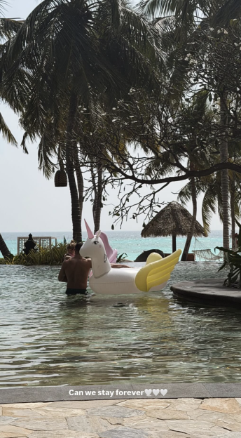A man standing in a pool next to a large unicorn float with the ocean in the background.