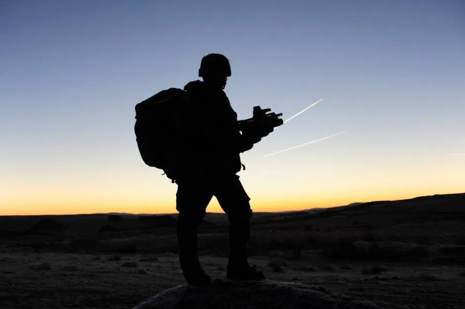 Silhouette of a British soldier in full gear on patrol at sunrise.