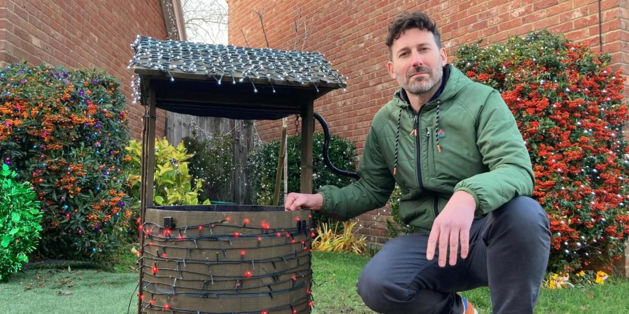A man kneeling next to a wishing well decorated with Christmas lights.