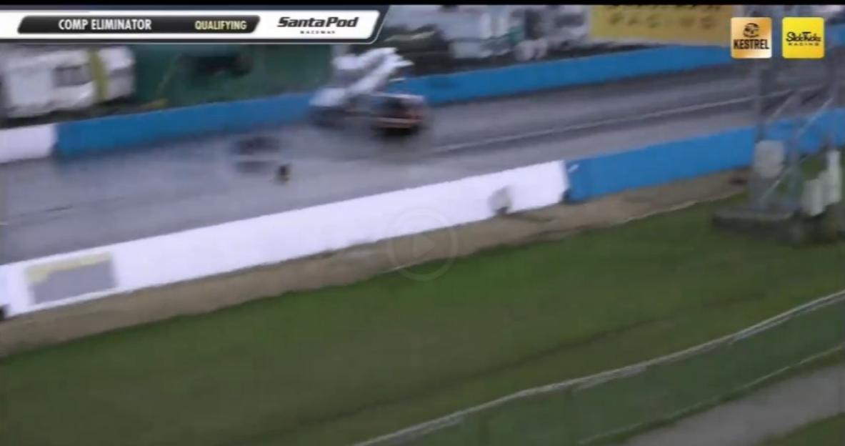 A drag racing car in motion on a wet track with water spraying from its tires.