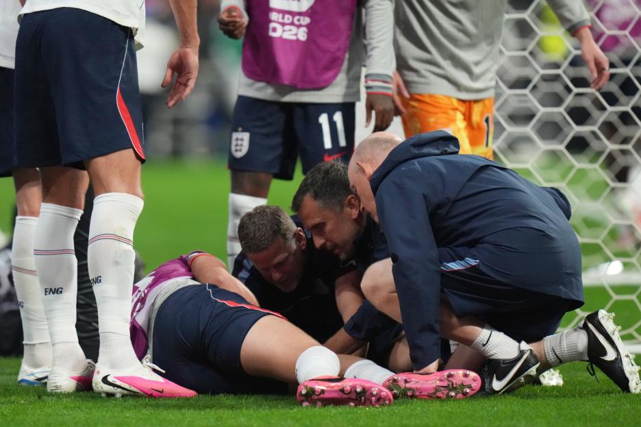 A player from England is on the ground receiving medical attention during a soccer match against Mexico.