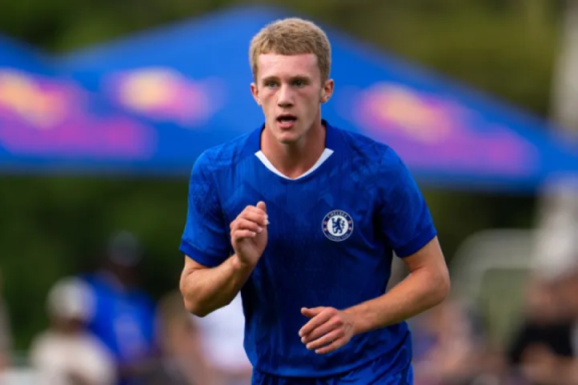 A young male soccer player with blond hair, wearing a blue Chelsea FC uniform, running on a field.