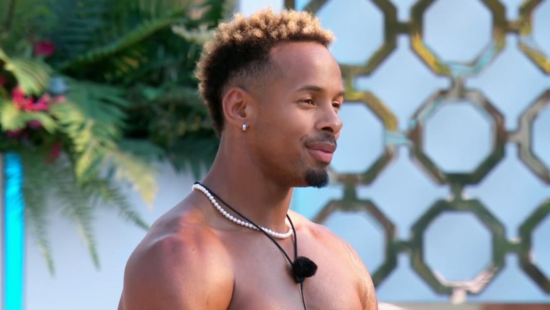 A man with a pearl necklace and an earring in his left ear looks to the right.