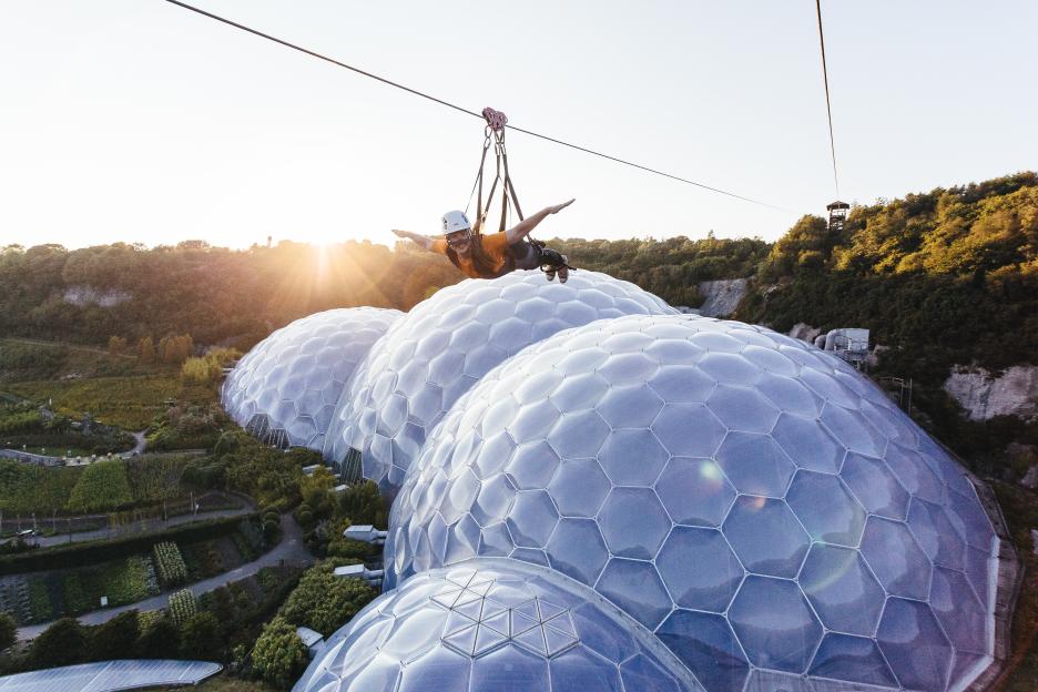 A person zip-lining over the Eden Project biomes at sunset.