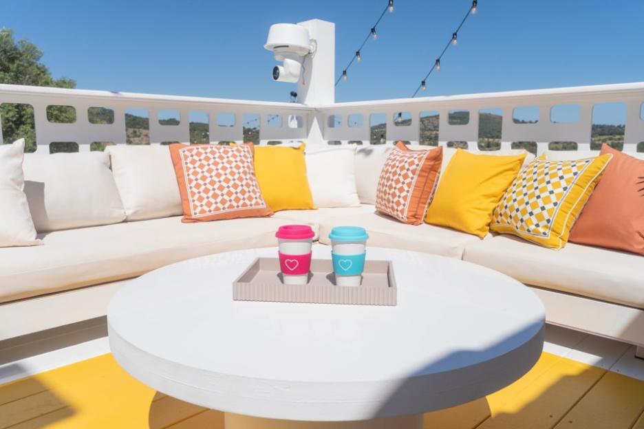 Outdoor patio with beige sofa, colorful pillows, and two cups on a table.