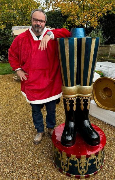 Man in a red Christmas-themed hoodie standing next to a large nutcracker decoration.
