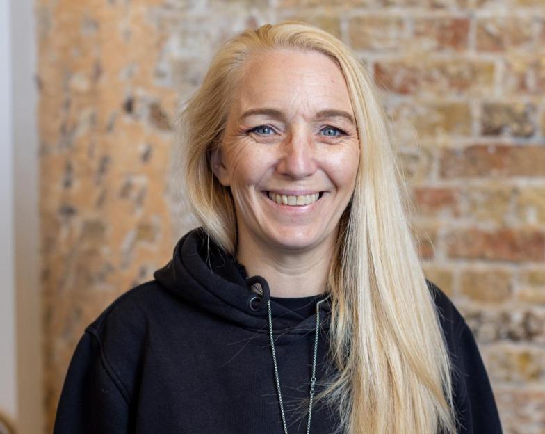 A smiling blonde woman with blue eyes wearing a black hoodie.