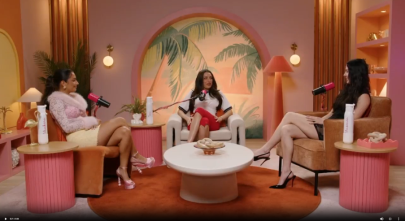 Three women sitting on armchairs in a podcast studio with colorful decor.