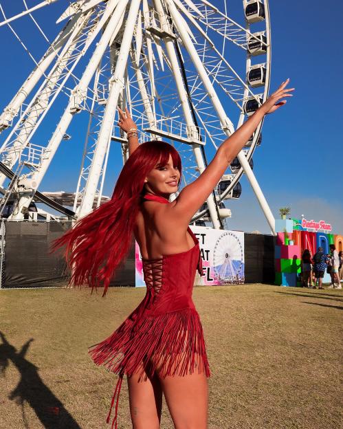 Maura Higgins with red hair and a red fringed dress with a Ferris wheel in the background at Coachella.