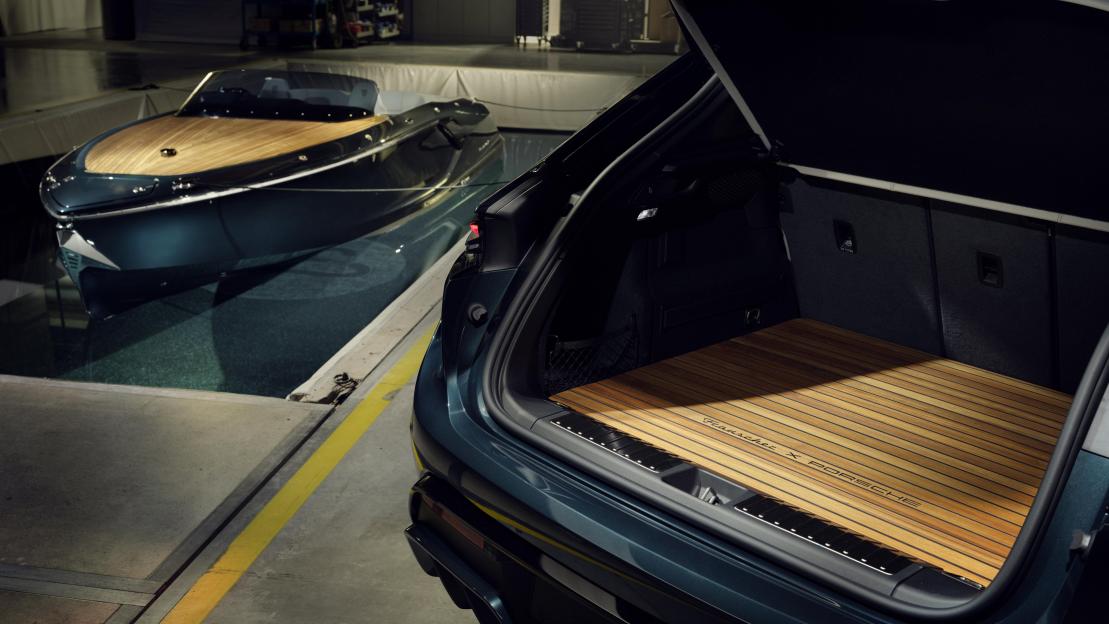 Open trunk of a dark green Porsche with a custom wooden floor, parked next to a matching boat with a wooden deck.