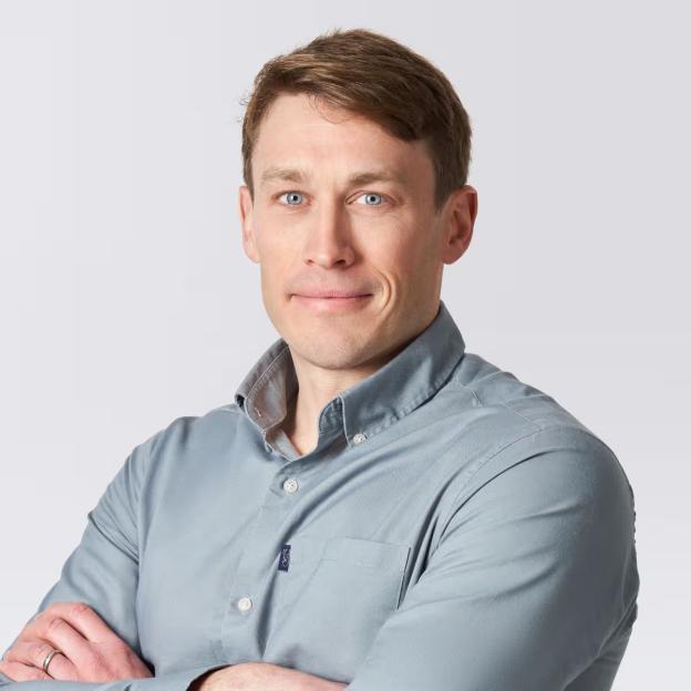 Dr. Adam Staten, GP, wearing a light blue button-up shirt with arms crossed.