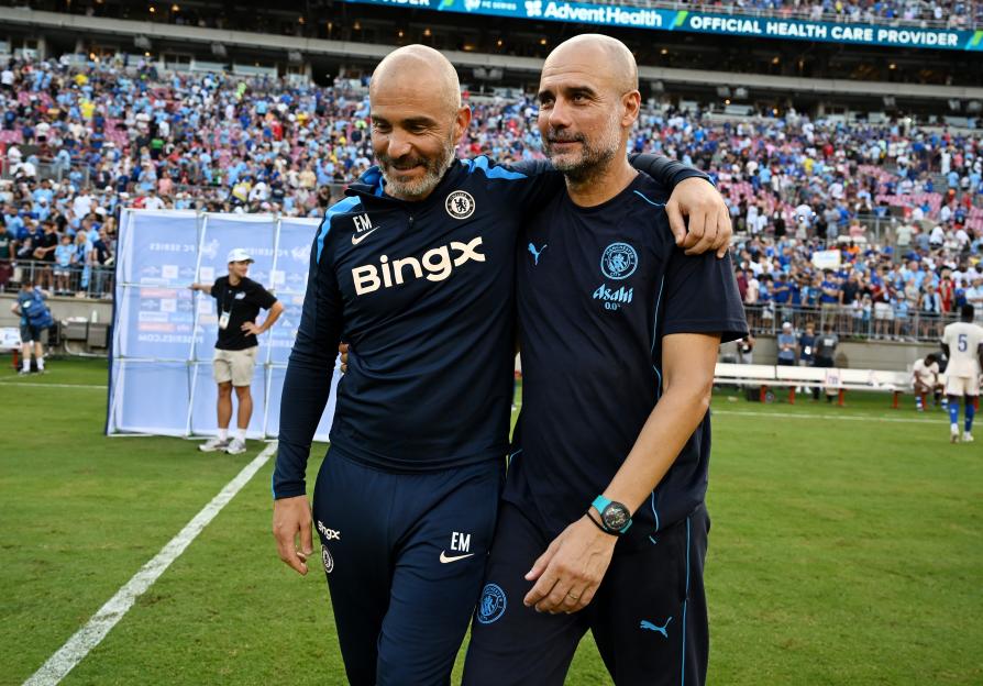 Chelsea manager Enzo Maresca and Manchester City manager Pep Guardiola standing with their arms around each other at a soccer game.