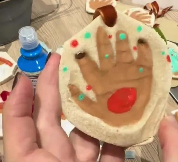 A person holding a salt dough Christmas ornament with a painted handprint and colorful dots.