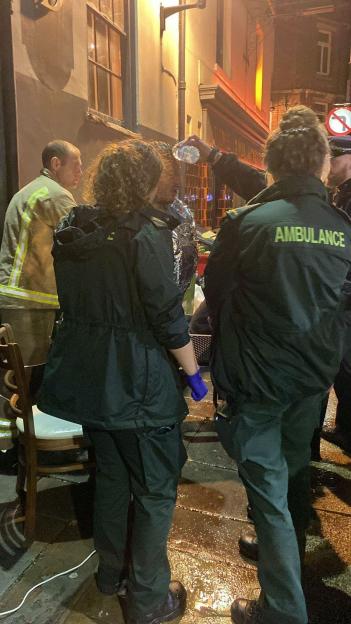 Paramedics and a firefighter treating a man doused in a substance, with an ambulance uniform visible in the foreground.