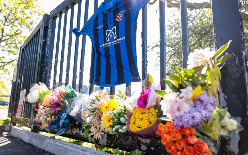 A black and blue striped football jersey hangs on a black metal fence above several bouquets of flowers.